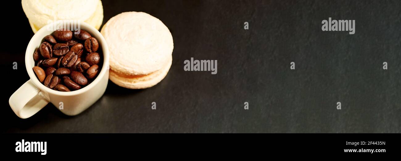 Tazza bianca con macaron dolci e chicchi di caffè sul tavolo. Intestazione Cafe e modello di sfondo Foto Stock