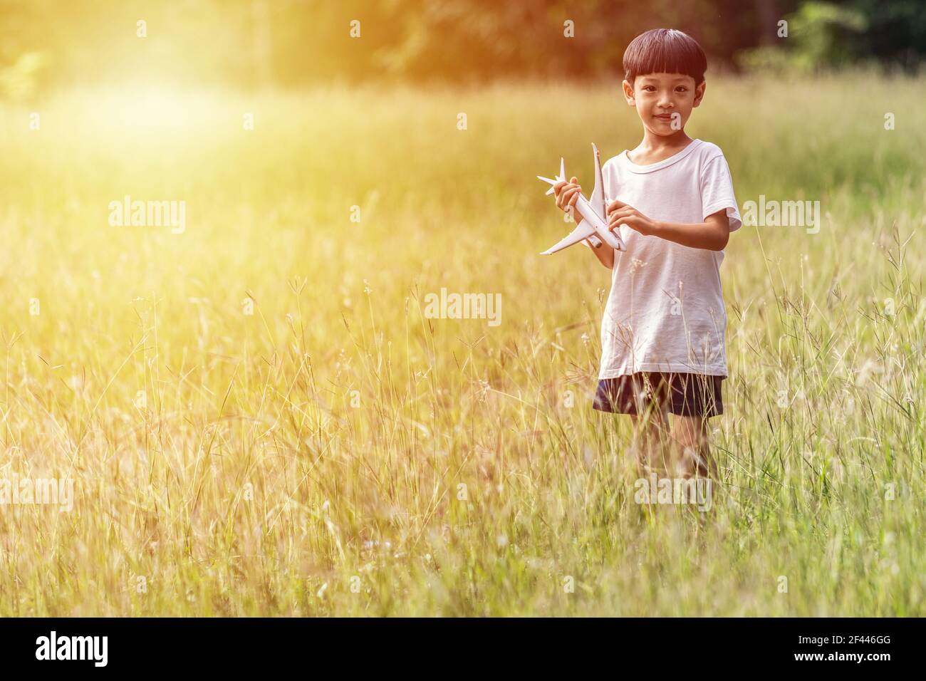 Carino bambino asiatico giocare aereo nel parco all'aperto felice ragazzo asiatico tenendo un aereo corre in un prato con il tramonto. Foto Stock
