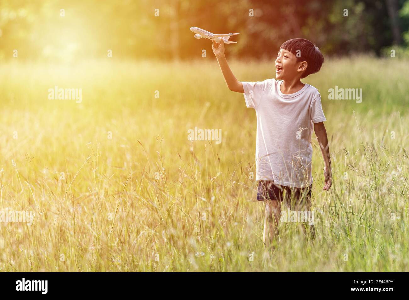 Carino bambino asiatico giocare aereo nel parco all'aperto felice ragazzo asiatico tenendo un aereo corre in un prato con il tramonto. Foto Stock