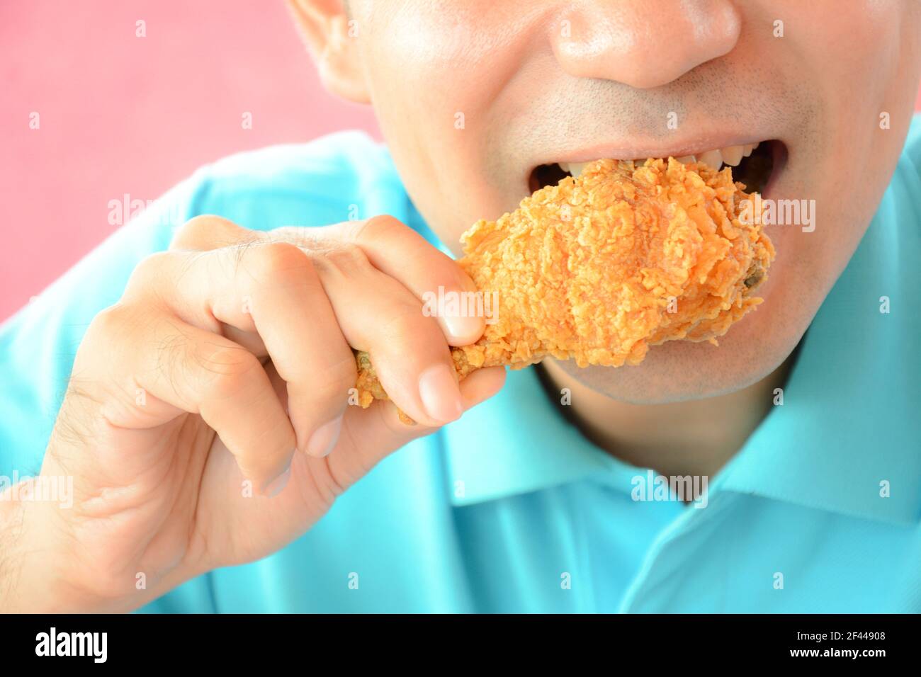 Un uomo che mordicchiava una coscia di pollo fritta o un bastone di pollo Foto Stock