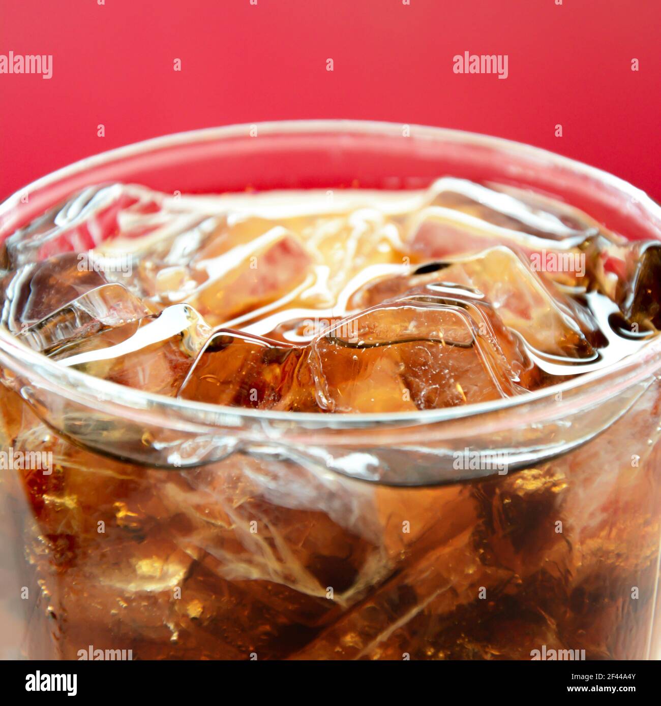Un bicchiere di bevanda analcolica alla cola con cubetti di ghiaccio sfondo rosso Foto Stock