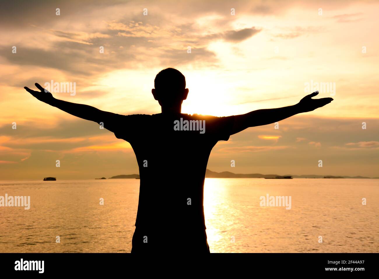 Silhouette di un uomo che alza le braccia su acqua di mare e cielo crepuscolo sfondo - felice, relax & successo concetto Foto Stock