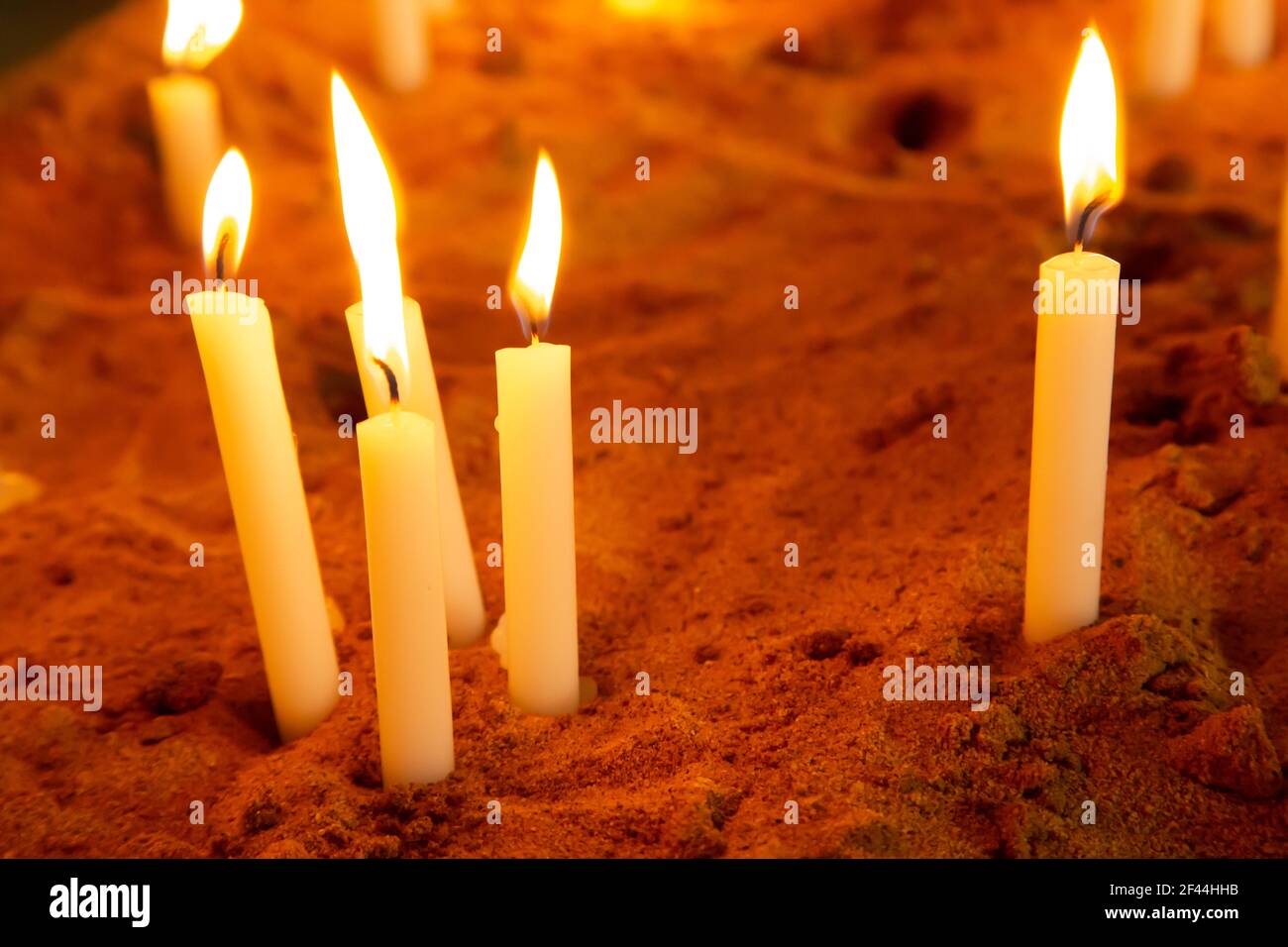 Un gruppo di candele di preghiera illuminate o accese in un scatola di sabbia Foto Stock