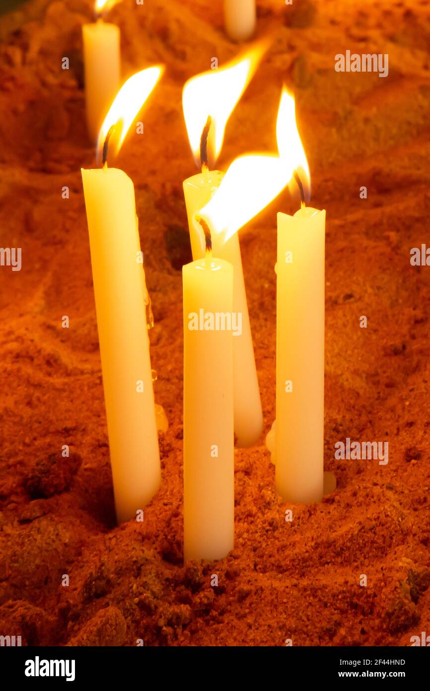 Un gruppo di candele di preghiera illuminate o accese in un scatola di sabbia Foto Stock