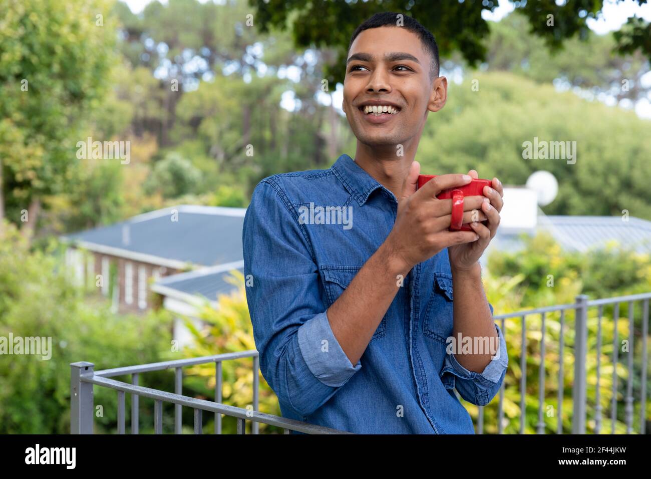 Uomo da corsa misto che beve caffè e sorridendo sul balcone Foto Stock