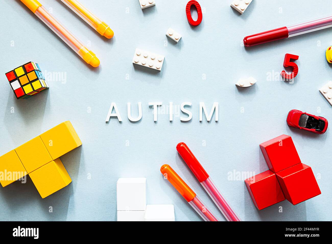 Giornata mondiale della consapevolezza dell'autismo. Piatto porre la parola bianca AUTISMO con cubi, puzzle, marcatori colorati e giocattoli sullo sfondo blu Foto Stock