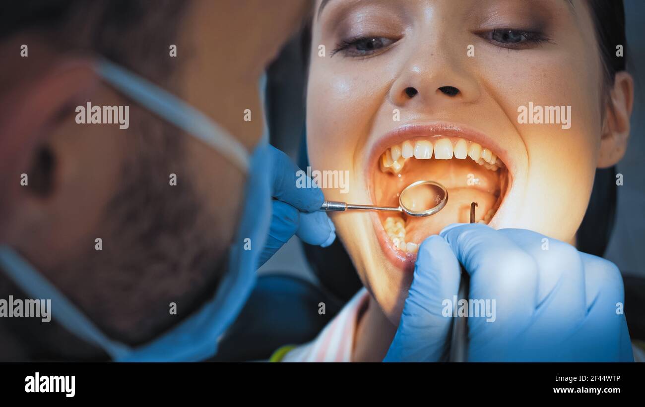 stomatologo in maschera medica che esamina i denti della donna, primo piano sfocato Foto Stock
