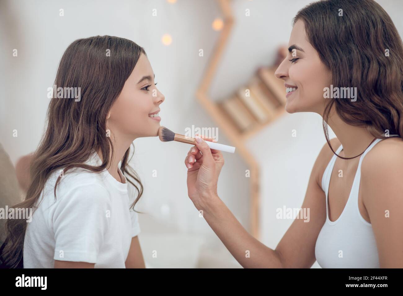 Mamma con spazzola per il trucco che tocca il mento della figlia adolescente Foto Stock