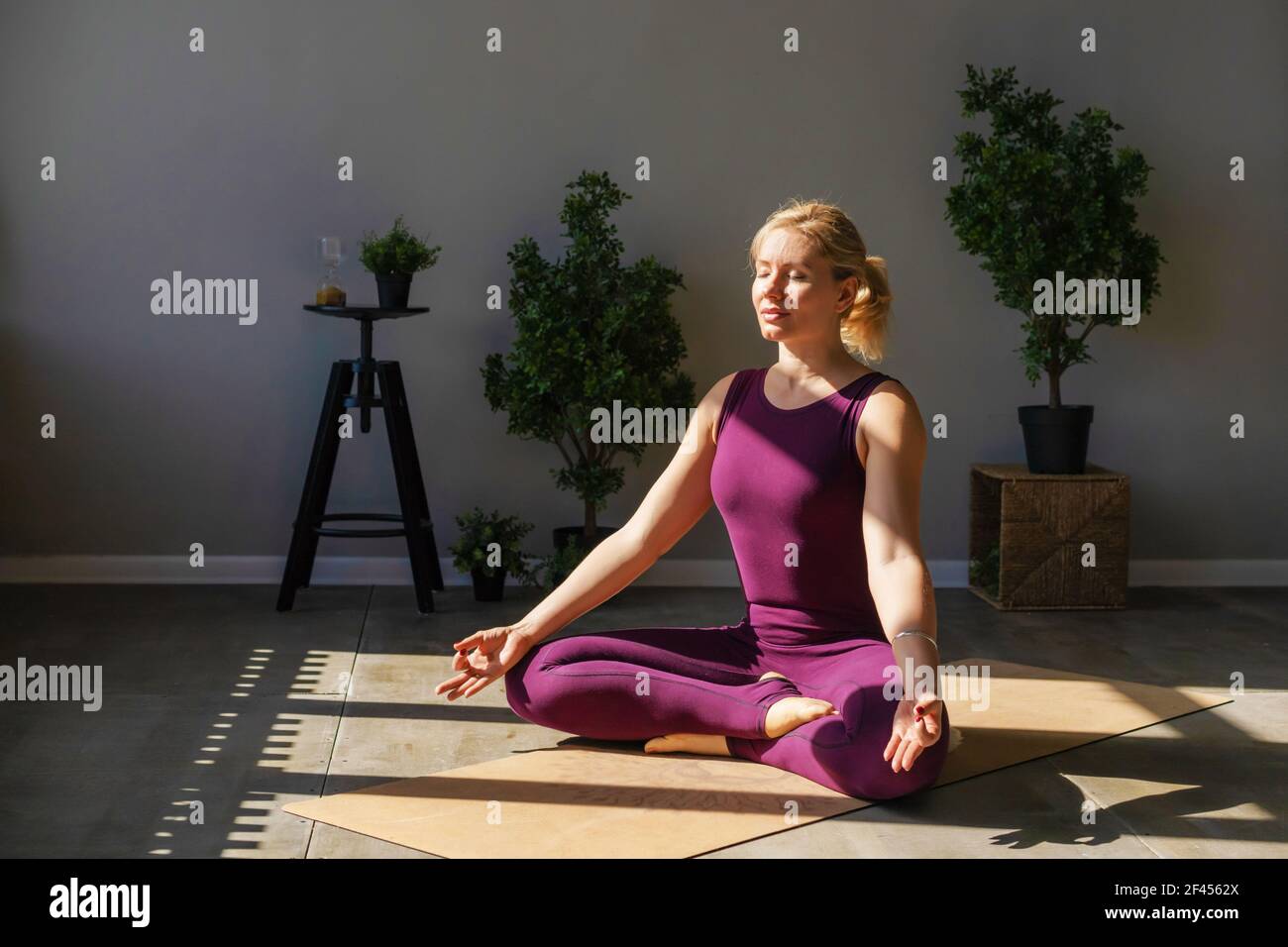Bella donna in abbigliamento sportivo seduta sul pavimento in lotus posizione meditazione a casa. Foto Stock