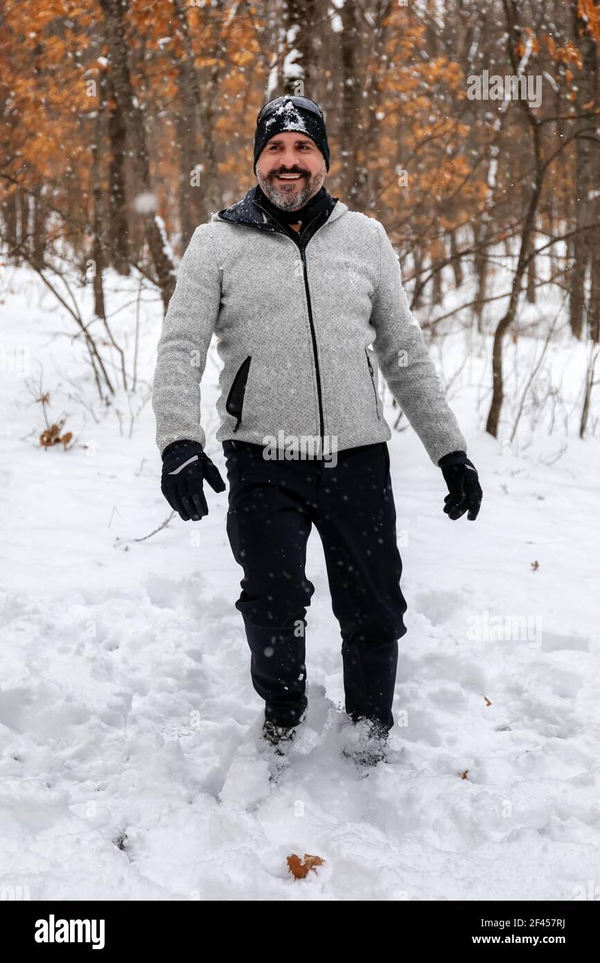 Un uomo bearded in abiti di montagna, felpa grigia, guanti e cappello nero,  immerso nella foresta innevata, gioisce per i fiocchi di neve che cadono  Foto stock - Alamy