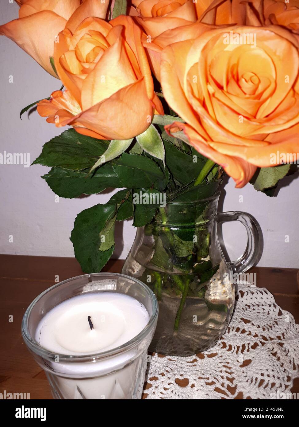 Colpo verticale di una candela e un bouquet di rose in un vaso sul tavolo Foto Stock