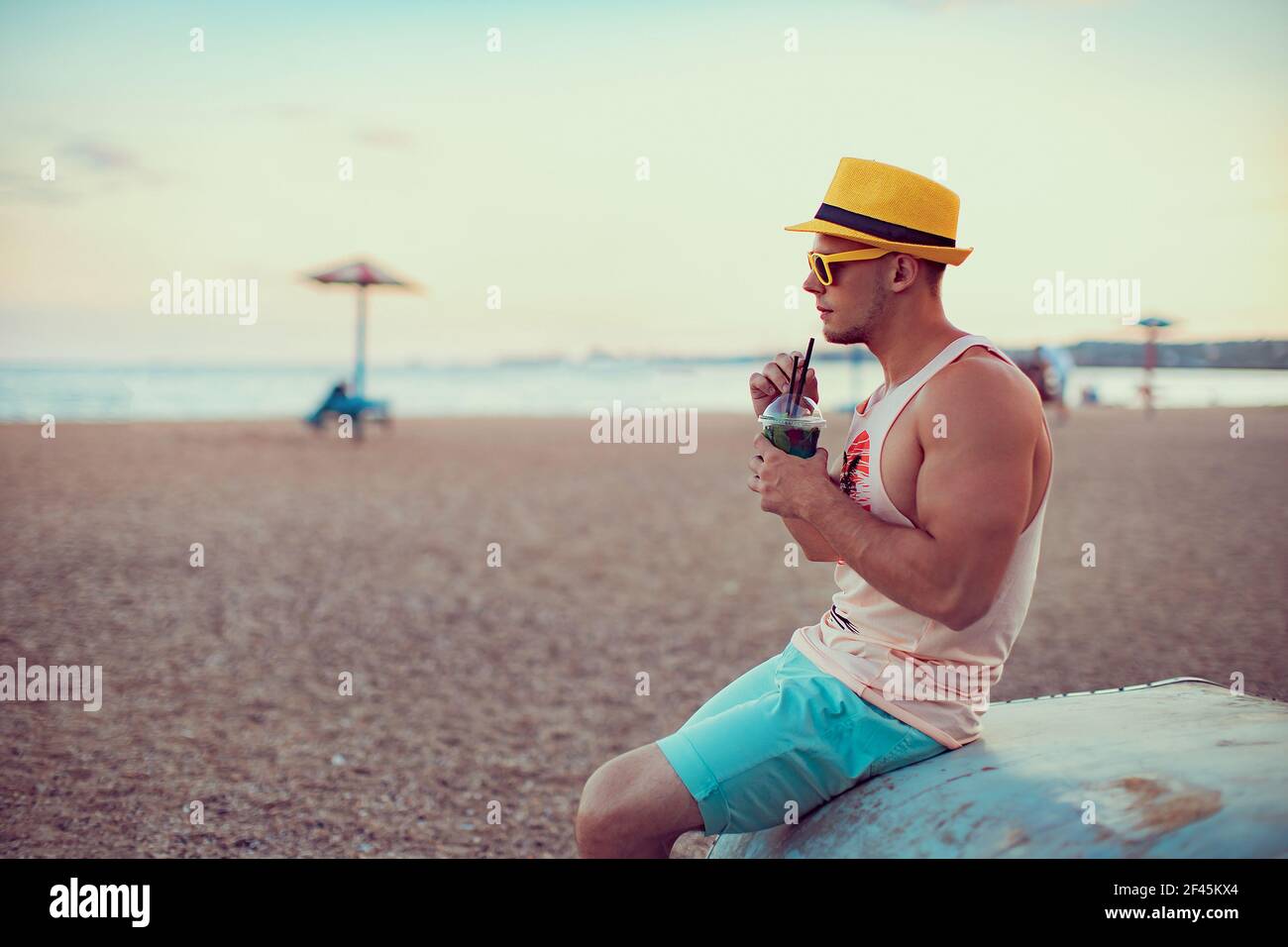 Giovane bell'uomo sportivo in abiti luminosi, cappello di paglia e occhiali  da sole si siede sulla riva, bere un cocktail rinfrescante e godersi la sua  vacanza Foto stock - Alamy