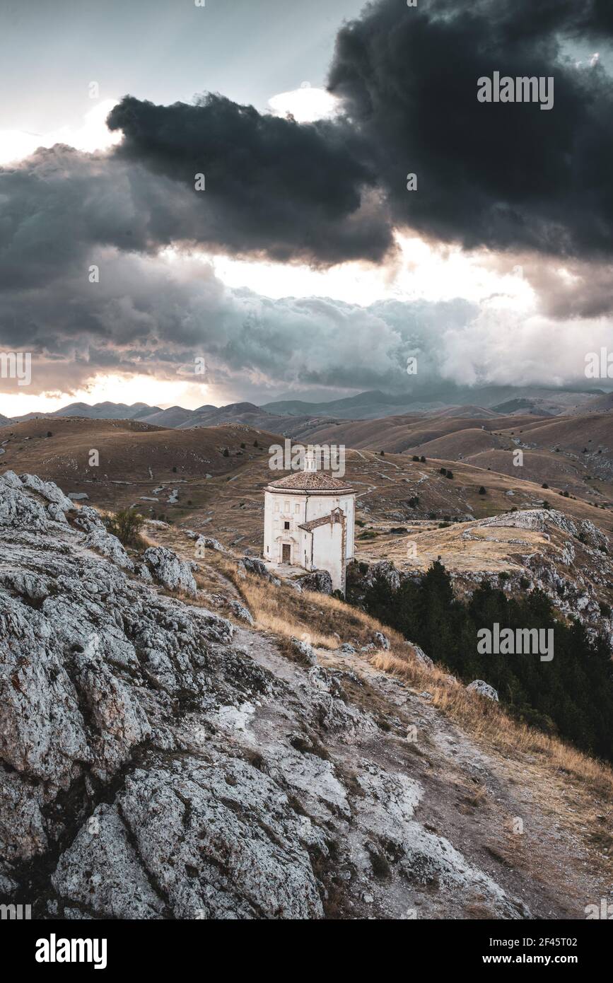 ITALIA, CALASCIO: Vista al tramonto sulla chiesa di Santa Maria della Pietà, situata nei pressi del castello medievale normanno di Calascio. Sullo sfondo, nascosto dietro le nuvole, il Monte Corno Grande. Foto Stock