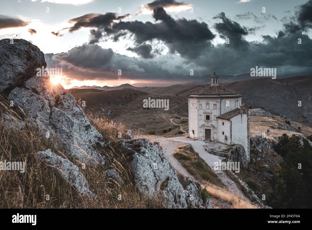 ITALIA, CALASCIO: Vista al tramonto sulla chiesa di Santa Maria della Pietà, situata nei pressi del castello medievale normanno di Calascio. Sullo sfondo, nascosto dietro le nuvole, il Monte Corno Grande. Foto Stock