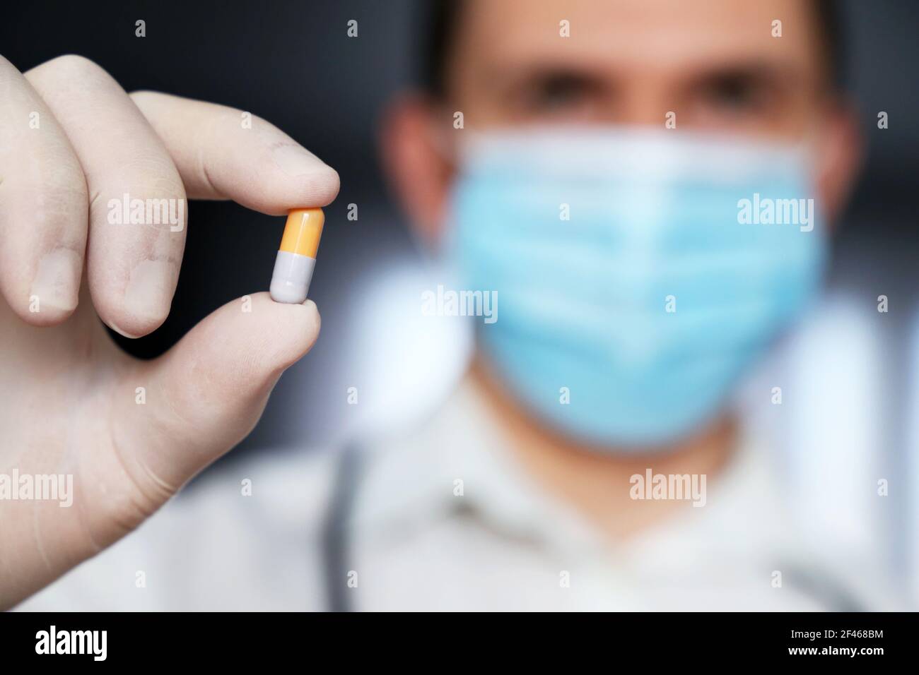 Farmaco in capsula in mano maschile vicino, medico in maschera medica tenendo pillola. Concetto di farmacia, farmaci, antibiotici o vitamine Foto Stock