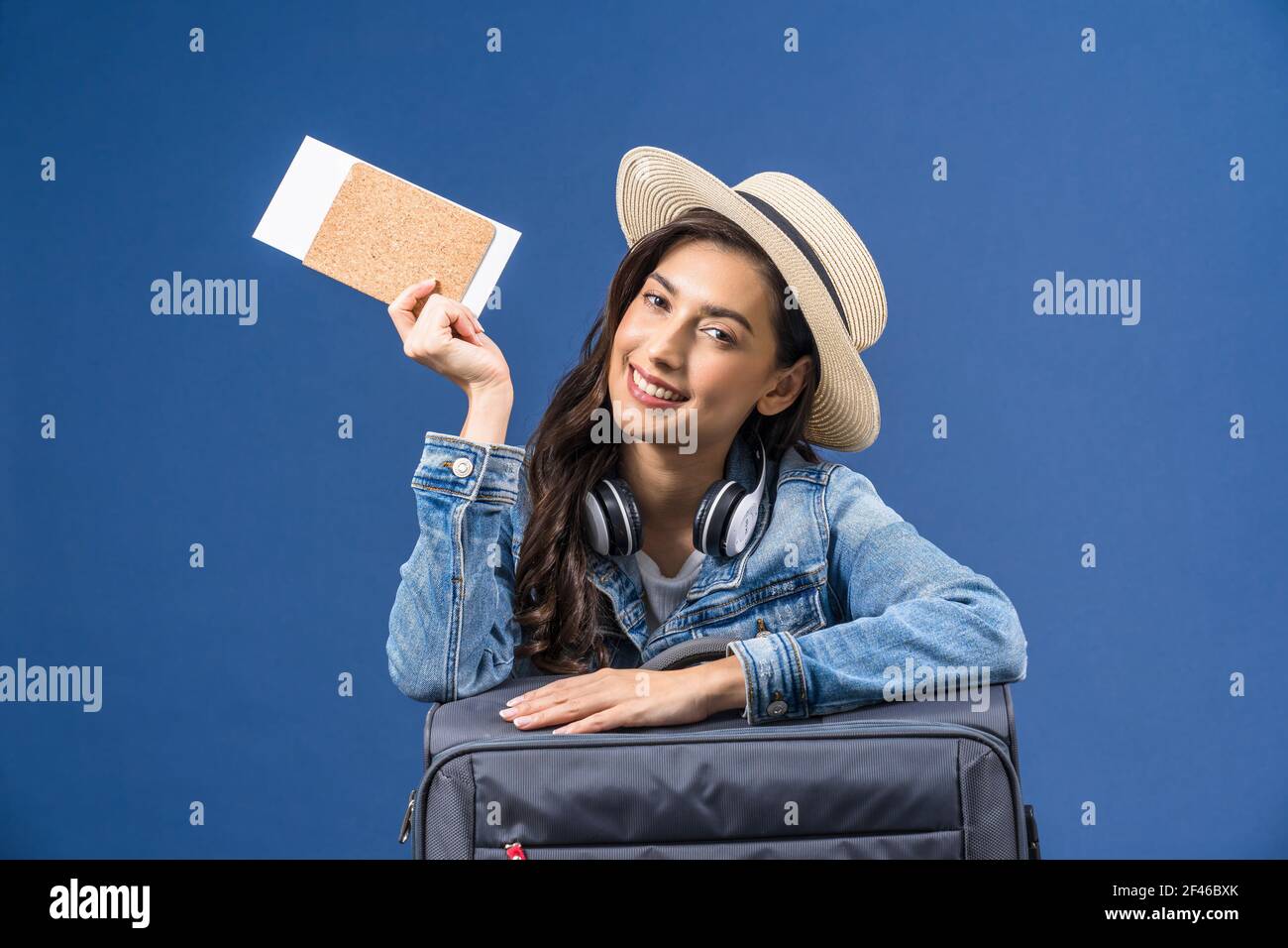 Felice giovane donna asiatica con passaporto con carta d'imbarco e presentazione su sfondo blu, auricolare e bagaglio, concetto di vacanza e viaggio Foto Stock Felice giovane donna asiatica con passaporto con carta d'imbarco e presentazione su sfondo blu, auricolare e bagaglio, concetto di vacanza e viaggio Foto Stock