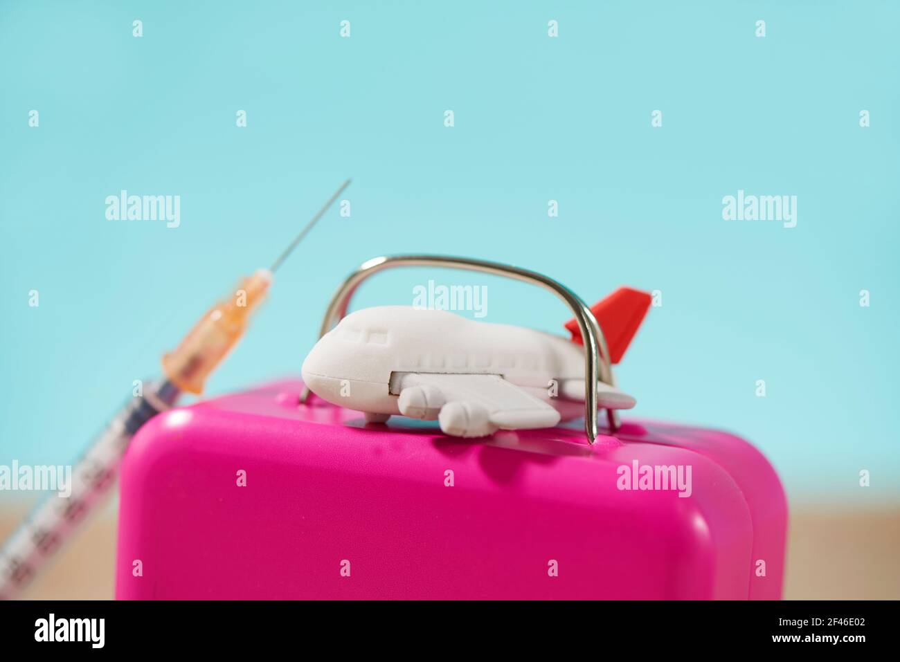 closeup di un aereo su una valigia rosa, e una siringa sulla sabbia, su uno sfondo blu, raffigurante il settore del turismo medico Foto Stock