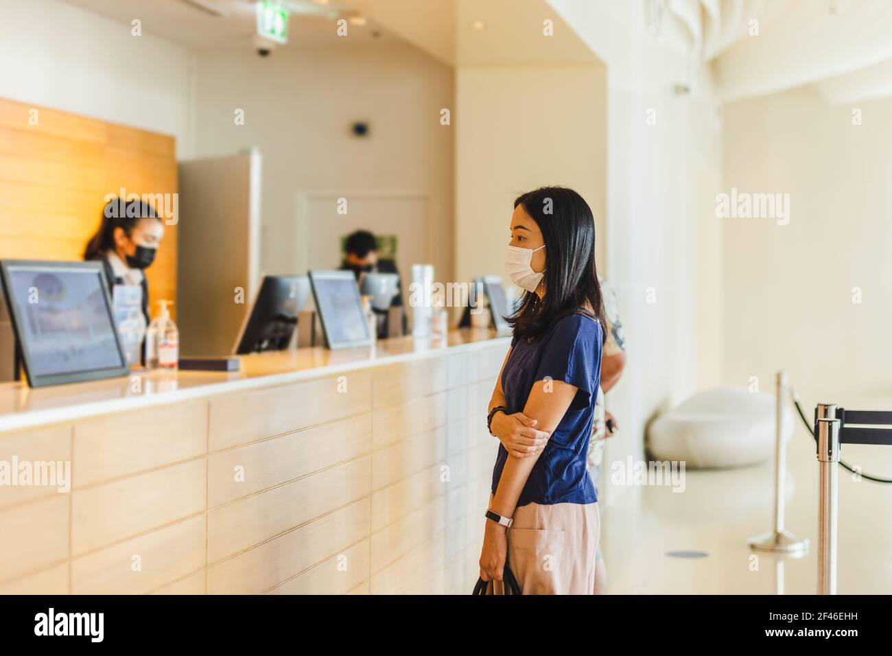 Donna turistica e receptionist al banco dell'hotel che indossa una maschera medica contro il virus. Foto Stock