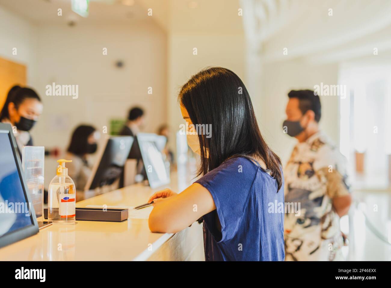 Ospite donna in maschera medica ckeck presso la reception dell'hotel. Foto Stock