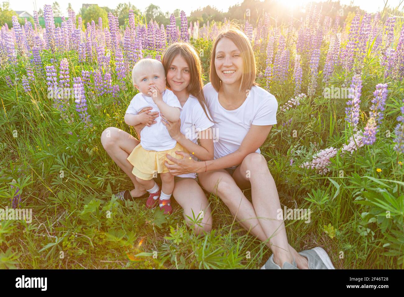 Giovane madre abbracciando i suoi bambini all'aperto. Donna bambino e adolescente ragazza seduta sul campo estivo con fiori selvatici fiore sfondo verde. Felice Foto Stock