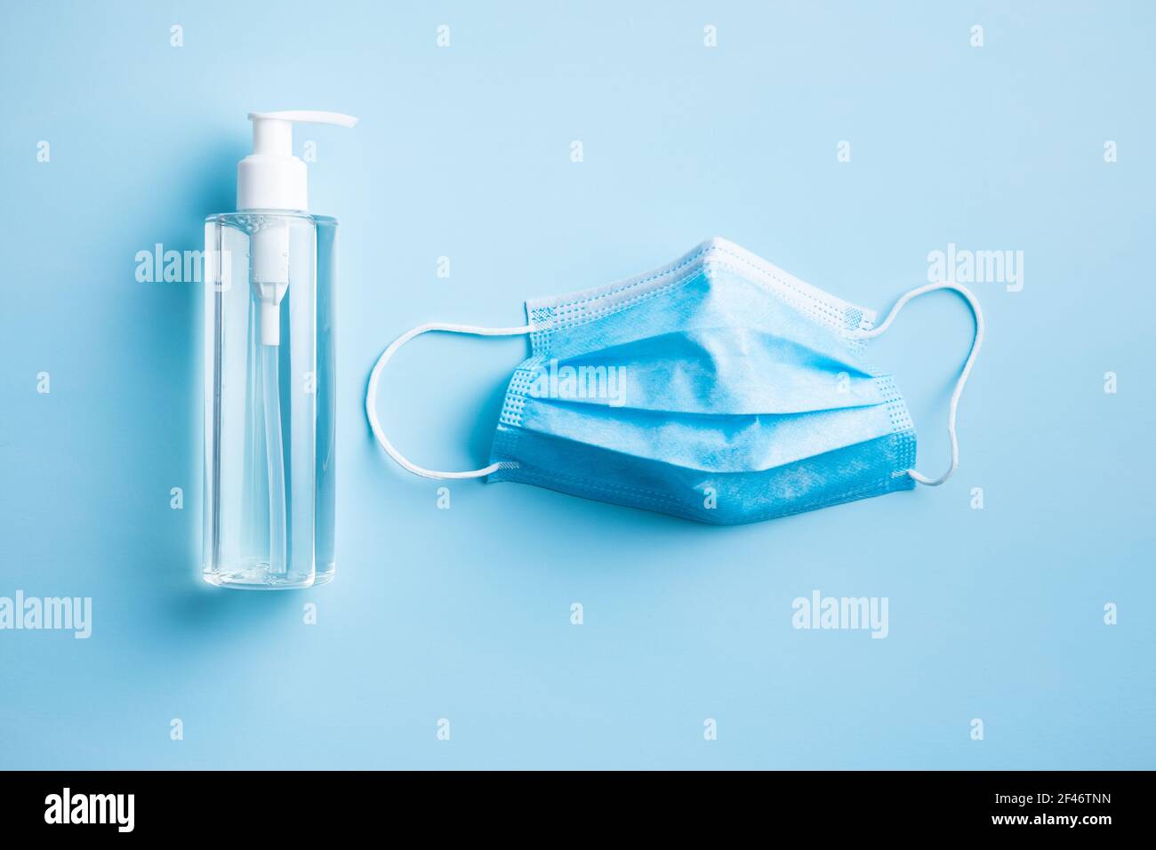 Disinfettante per le mani e maschera medica per la prevenzione del coronavirus. Gel disinfettante per le mani nel flacone della pompa sul tavolo blu. Vista dall'alto. Foto Stock