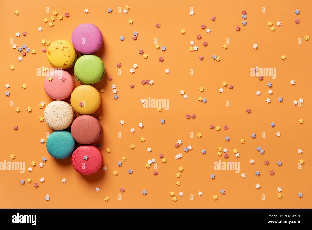 Set di macaroni multicolore su sfondo arancione con piccole stelle. Mockup del biglietto d'auguri con dolci torte di macaron multicolore. Dessert francese. Foto Stock