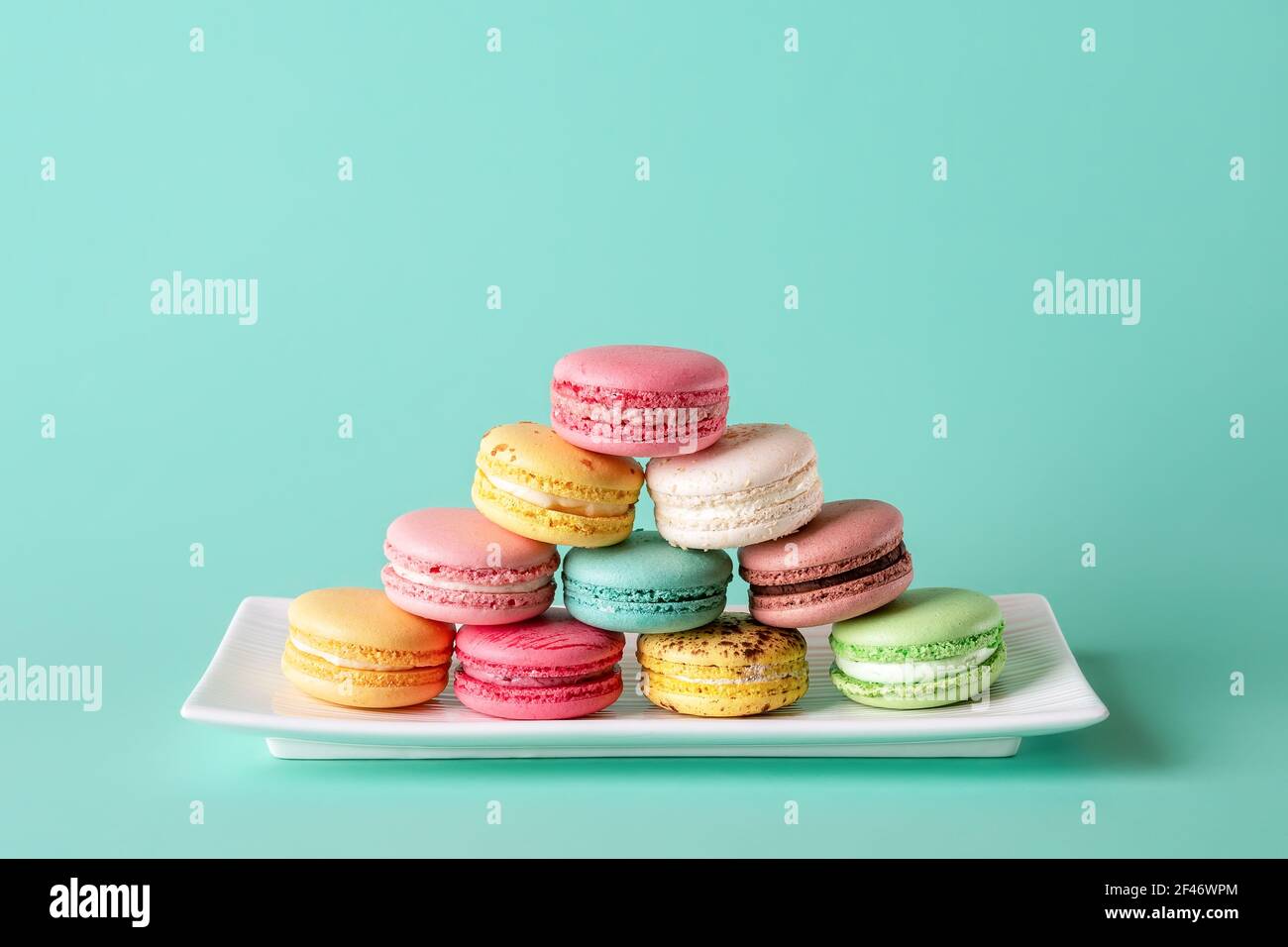 Colorata piramide di macaroni su una piastra rettangolare bianca su sfondo color turchese pastello. Mockup di biglietto d'auguri con macaron dolci multicolore. Foto Stock