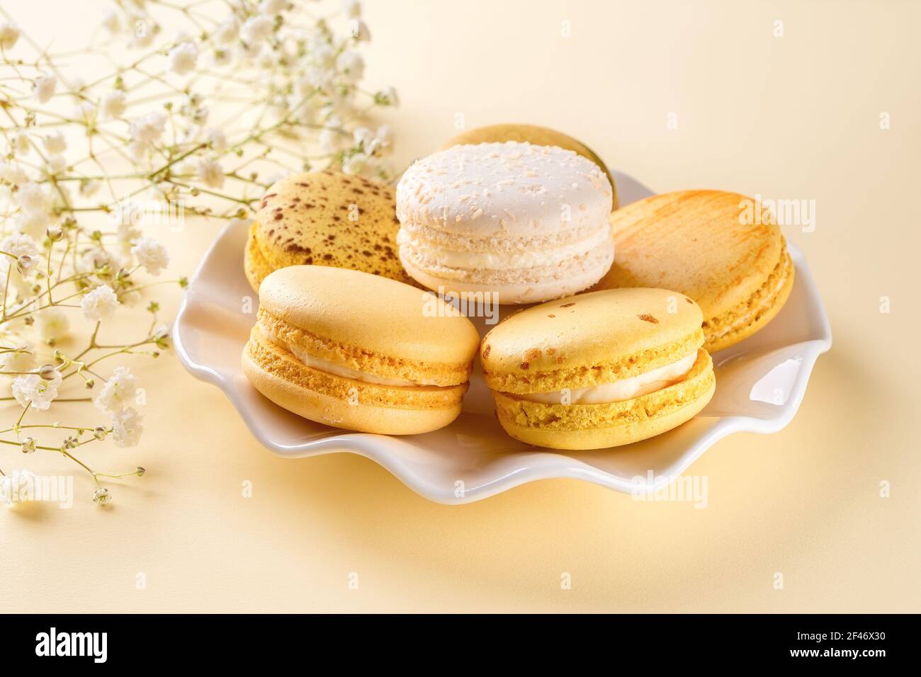 Amaretti gialli su un piatto bianco elegante su sfondo giallo pastello. Colazione dolce con deliziosi biscotti alla meringa di mandorle. Primo piano. Foto Stock