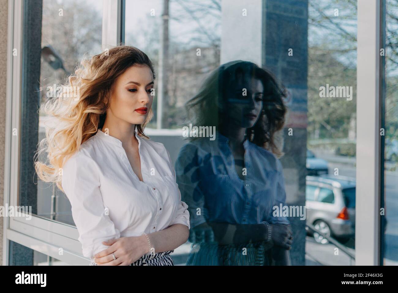 Salute mentale delle donne. Ansia disturbi panici. Disturbo bipolare. Ritratto esterno della giovane triste donna e il suo riflesso scuro nella finestra a specchio Foto Stock