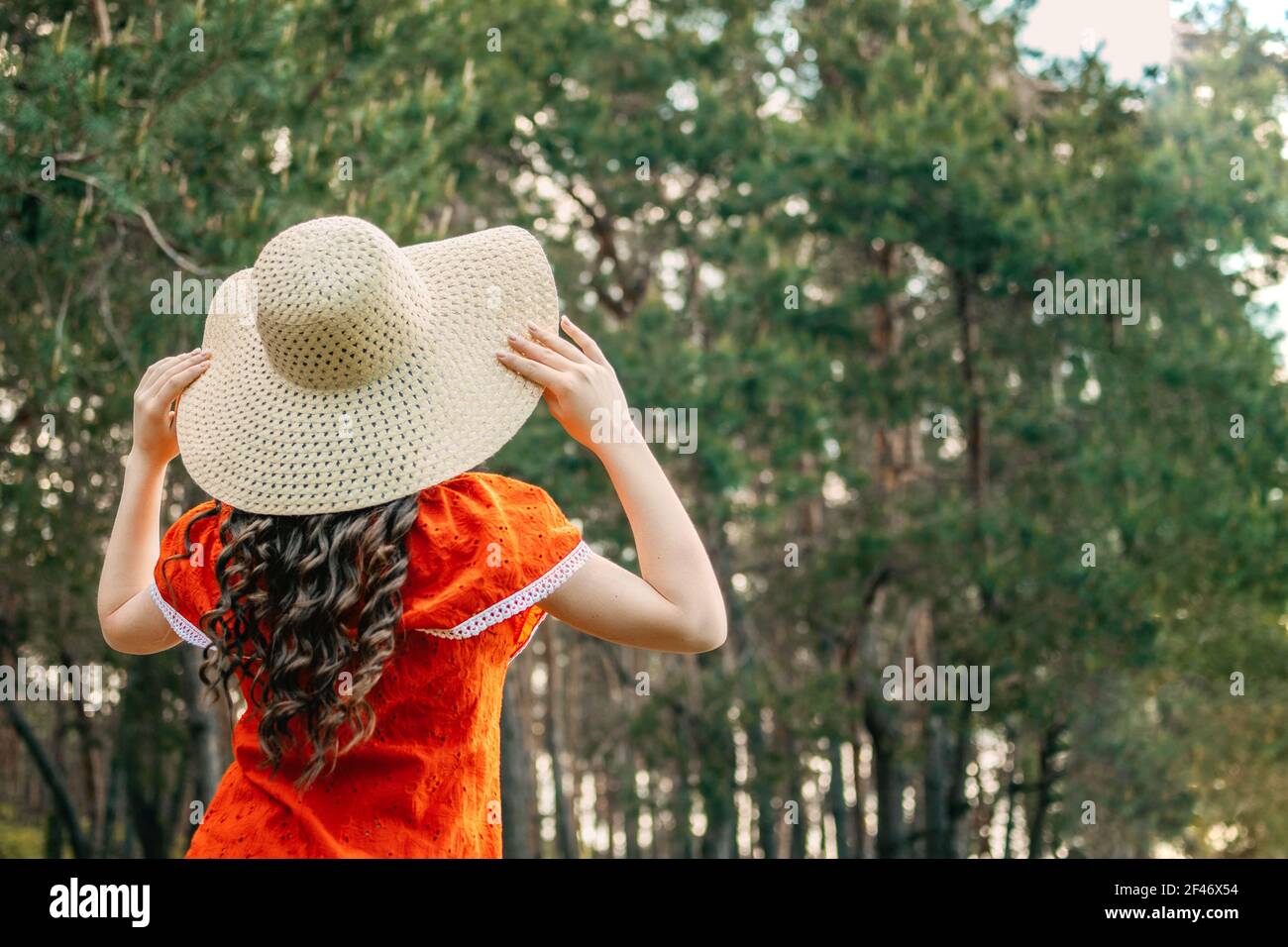 Godere della natura, benessere, benessere, stile di vita sano, vita lenta. Giovane bruna ragazza in abito rosso e cappello di paglia che cammina nella foresta, boschi. Foto Stock