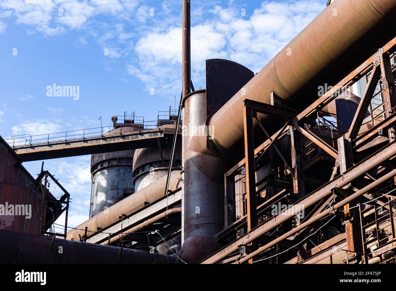 Vista verso l'alto di un vecchio impianto di acciaieria, labirinto di tubi e altiforni, cielo blu, aspetto orizzontale Foto Stock