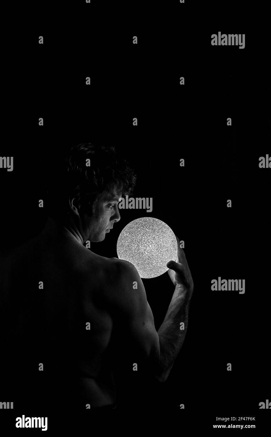 un'immagine verticale di un maschio dal lato destro tenere una luce rotonda nel buio Foto Stock