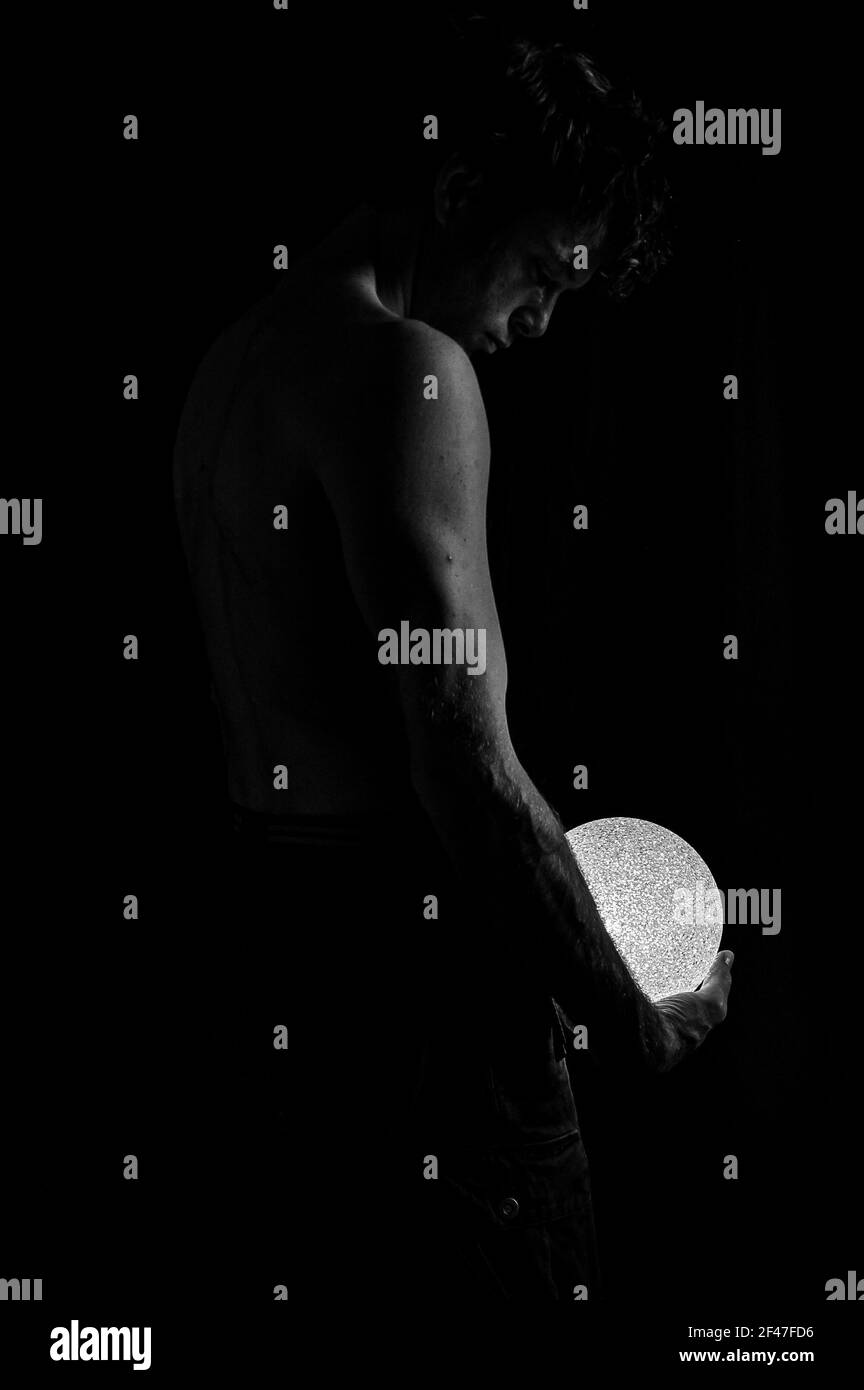 un'immagine verticale di un maschio dal lato destro tenere una luce rotonda nel buio Foto Stock