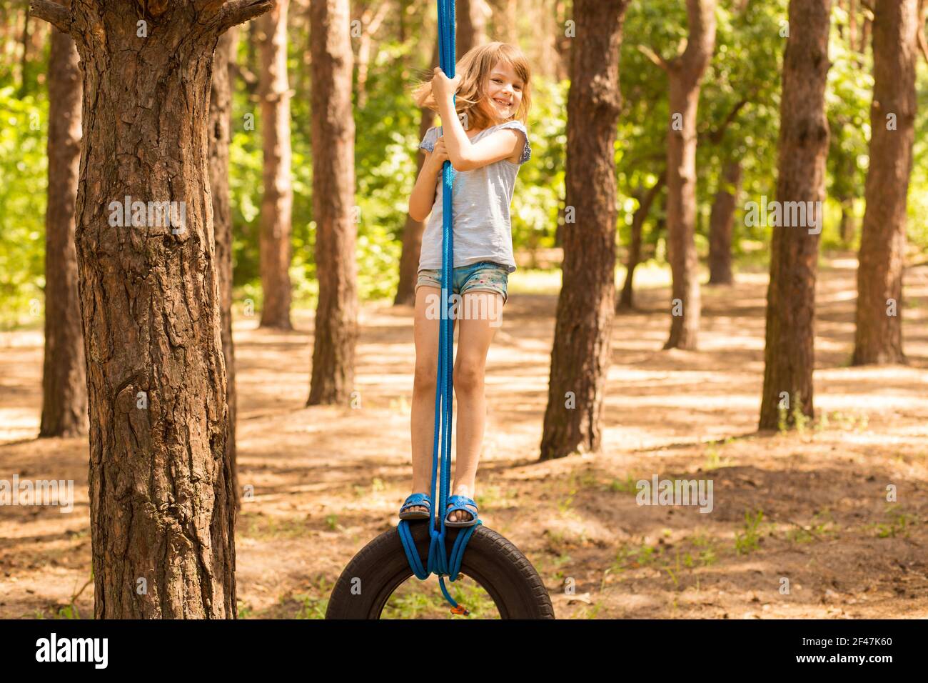 Carino bambina che oscilla sulla ruota attaccata al grande albero nella foresta di autunno. Foto Stock