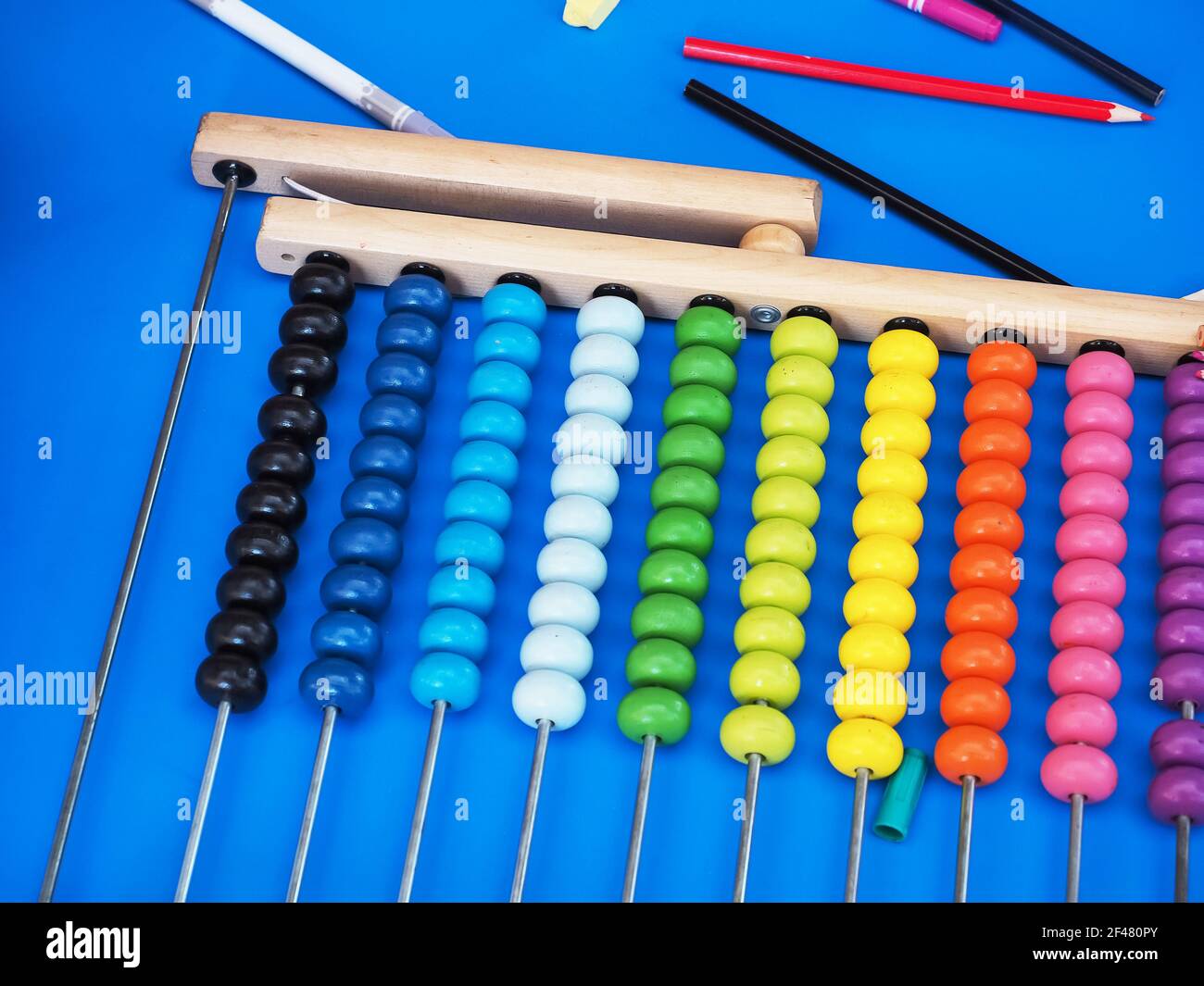 Abaco di legno con perline multicolore su superficie blu brillante tra matite colorate Foto Stock