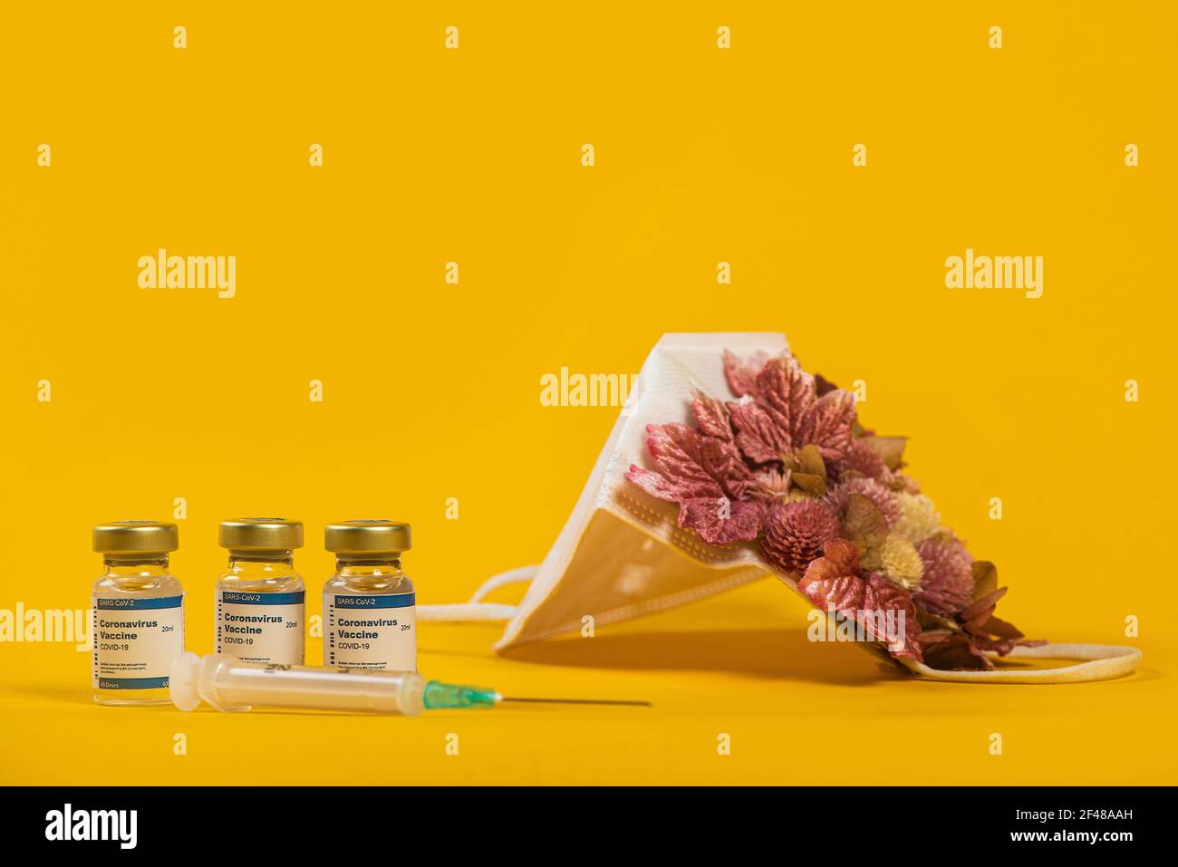 Tre flaconcini di Coronavirus e siringa con maschera medica per il viso con fiori rosa su di esso. Concetto creativo di influenza stagionale, allergie o coronavirus. Foto Stock