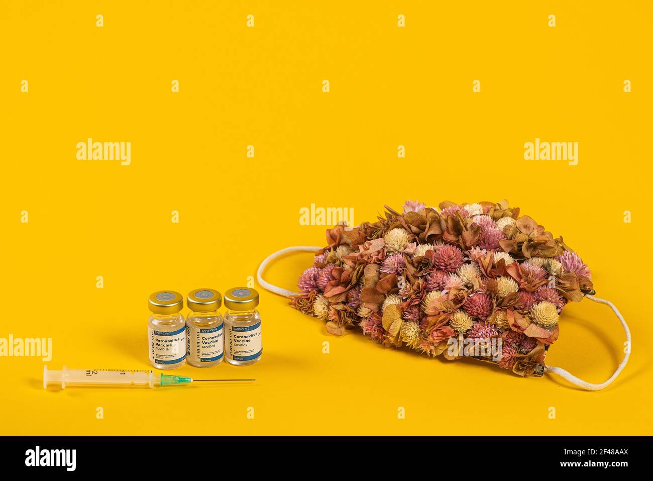 Tre flaconcini di Coronavirus e siringa con maschera medica per il viso con fiori rosa su di esso. Concetto creativo di influenza stagionale, allergie o coronavirus. Foto Stock