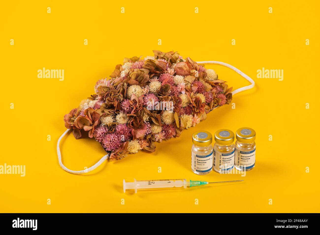 Tre flaconcini di Coronavirus e siringa con maschera medica per il viso con fiori rosa su di esso. Concetto creativo di influenza stagionale, allergie o coronavirus. Foto Stock