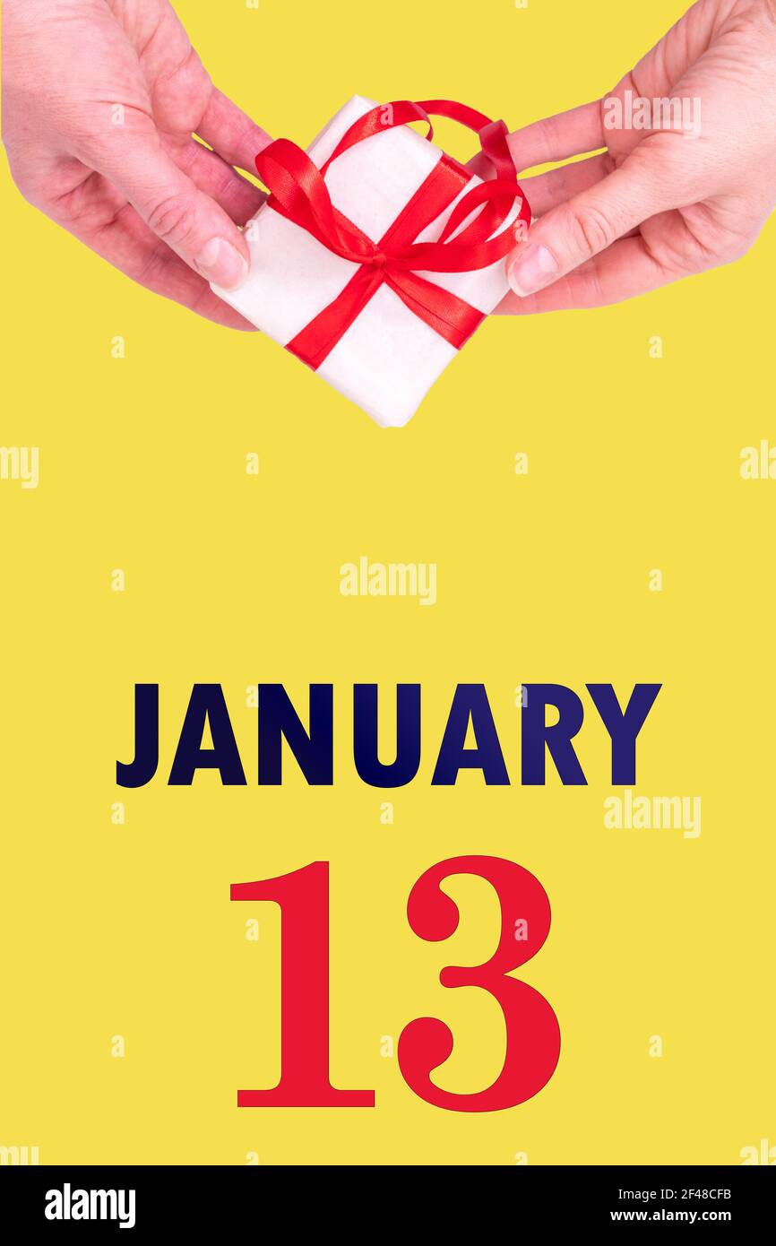 13 gennaio. Calendario verticale festivo con mani che tiene Bianco scatola regalo con nastro rosso e calendario Data 13 gennaio su illuminante Backgrou giallo Foto Stock