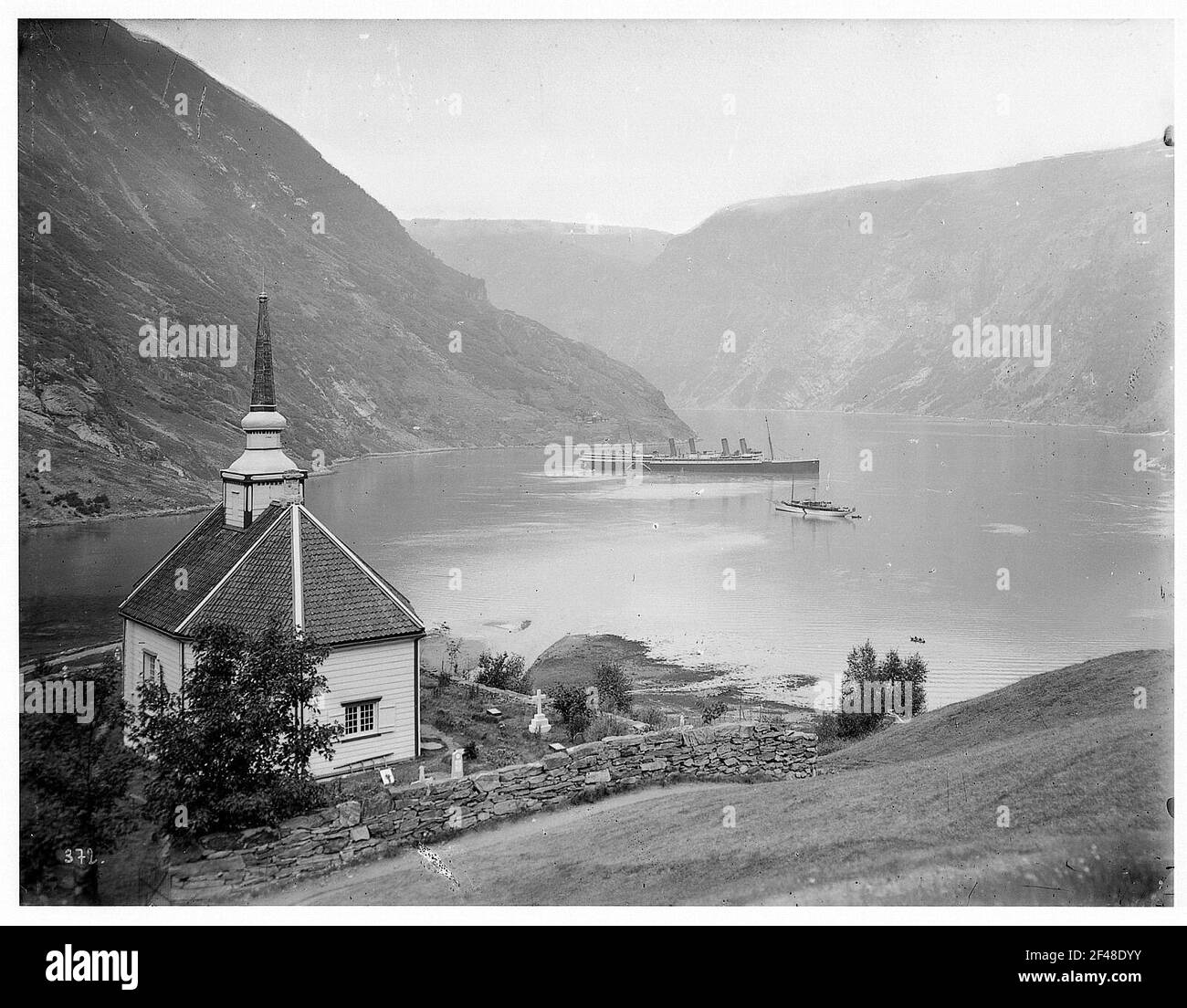 Merok. Vista sul luogo con la chiesa e il cimitero al Geirangerfjord con un passeggero a vapore Foto Stock