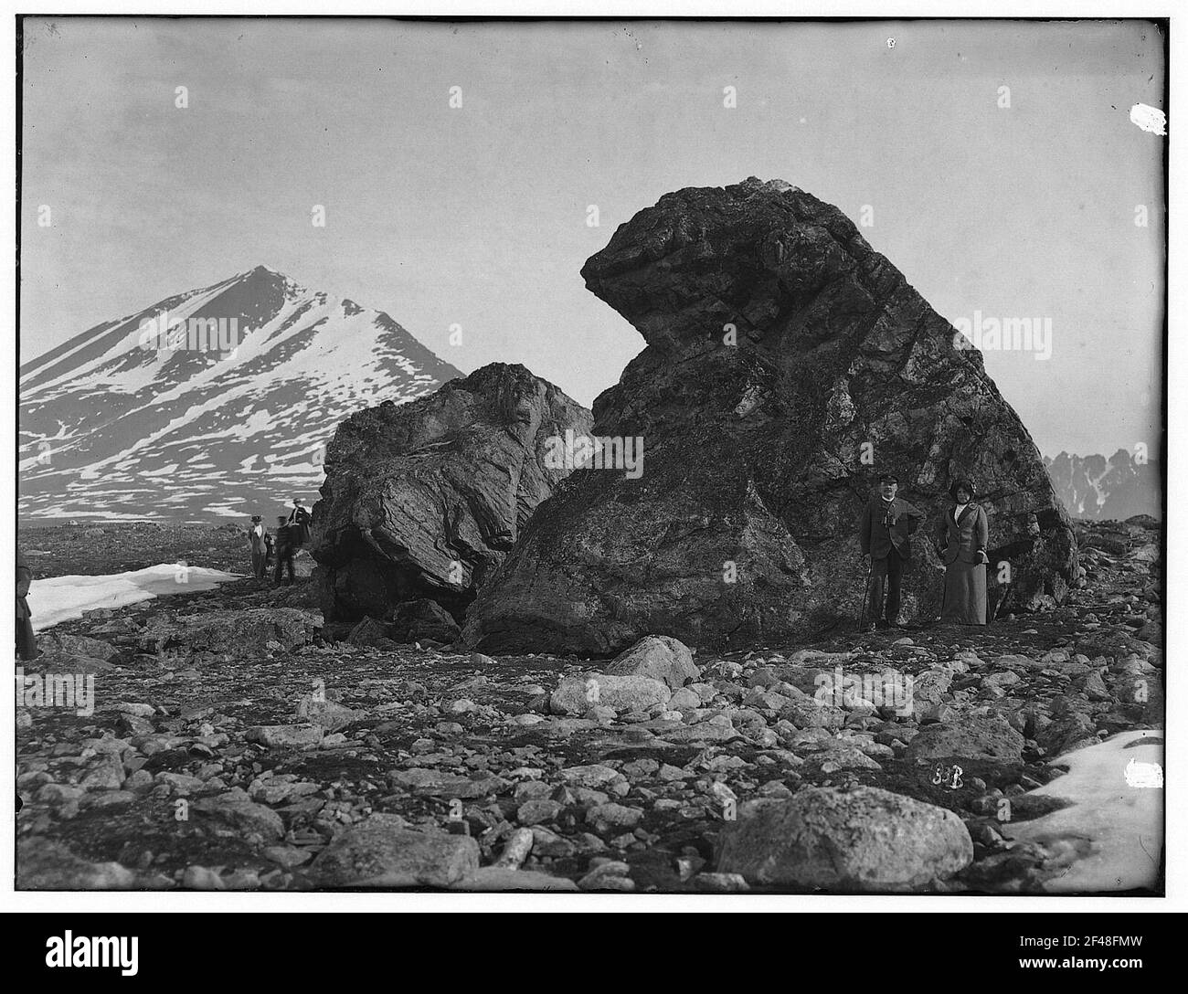Coppia turistica in posa contro formazioni rocciose sulla piana riva di crossfiordo contro le montagne innevate Foto Stock