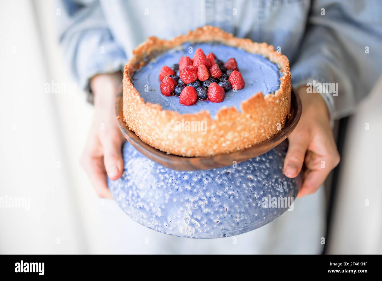 Donna che tiene la cheesecake di bacche su un bel supporto blu, primo piano Foto Stock