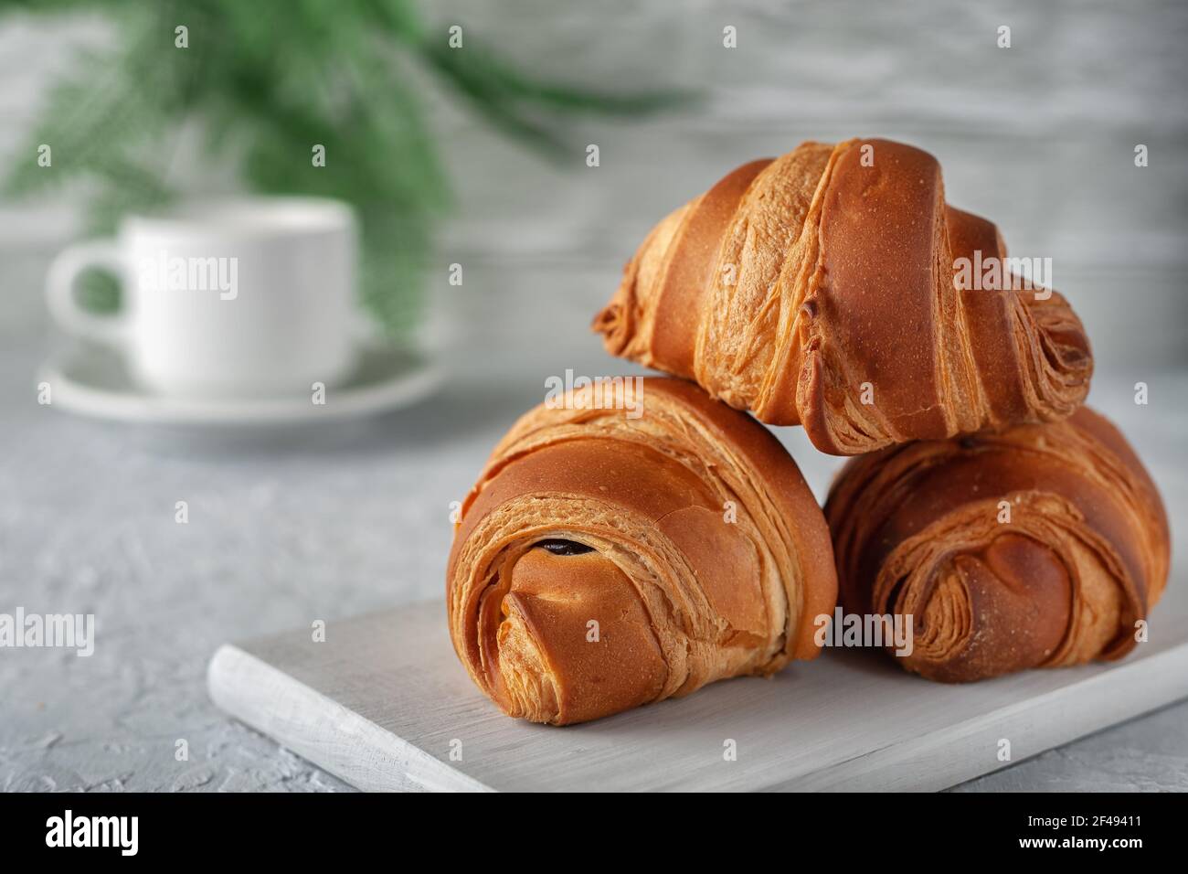 Su uno sfondo chiaro, un croissant appena sfornato con una tazza di latte Foto Stock