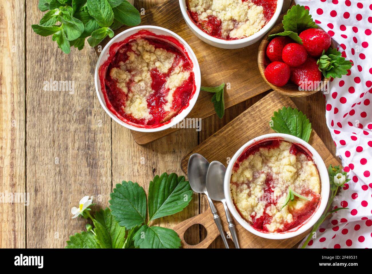 Dessert estivo cucina casalinga. Fragole sbriciolare in una teglia e fragole fresche su un tavolo rustico in legno. Vista dall'alto in piano. Spazio di copia. Foto Stock
