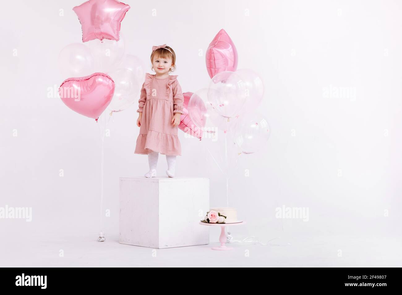 buon compleanno bambina di 2 anni in abito rosa. torta bianca con candele e  rose. Decorazioni di compleanno con palloncini bianchi e rosa e c Foto  stock - Alamy