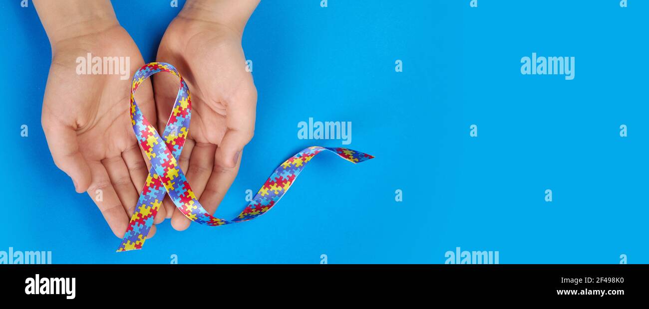 Giornata mondiale di consapevolezza dell'autismo. Mani autistico ragazzo tenendo nastro modello puzzle su sfondo blu Foto Stock
