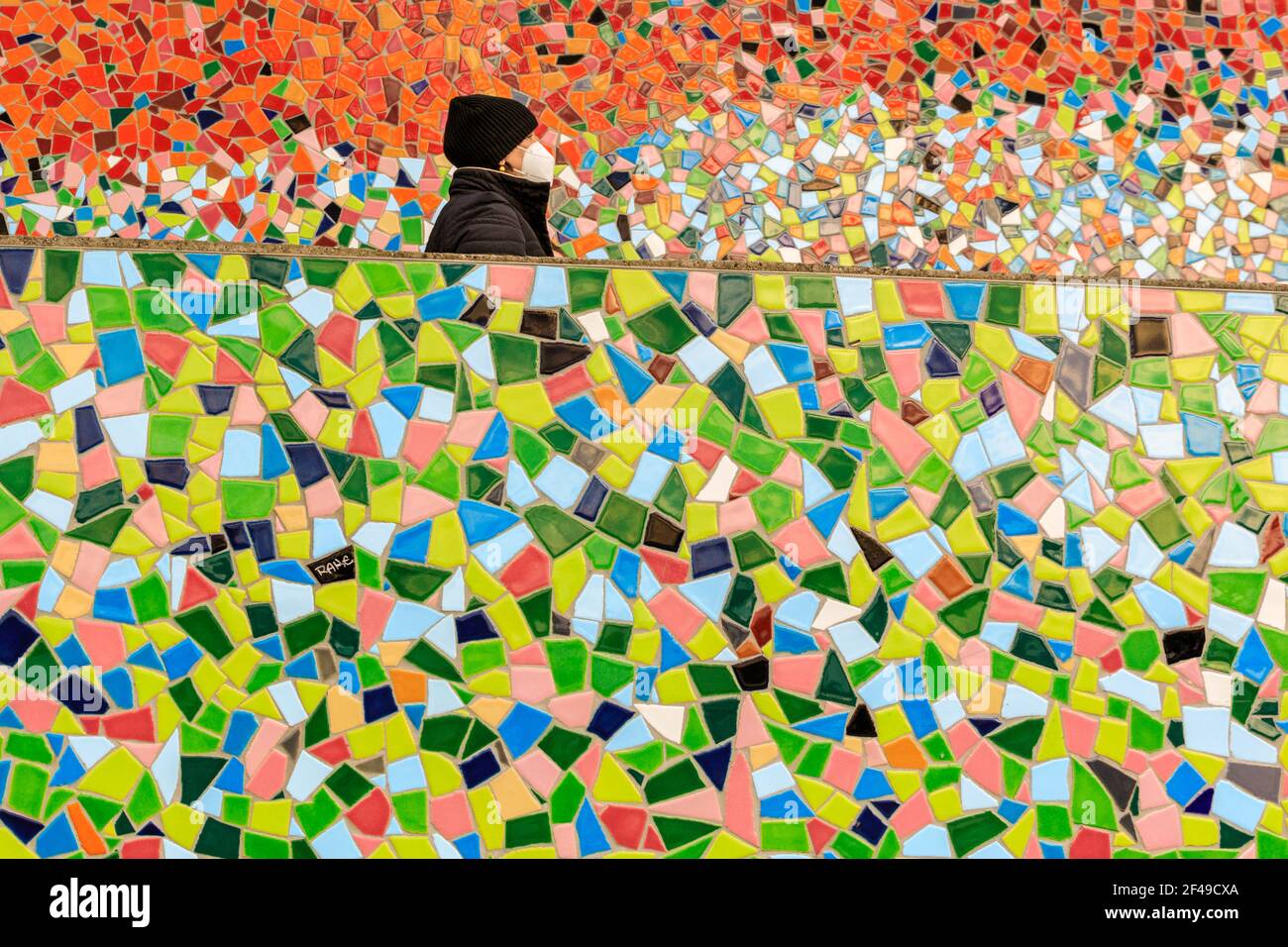 Dusseldorf, NRW, Germania, 19 marzo 2021. Una donna in maschera facciale FFP2/KN95 passa accanto alla parete a mosaico 'Rivertime' di Hermann-Josef Kuhna, sulle rive del fiume Reno a Dusseldorf, capitale della NRW. È probabile che le misure di blocco aumenteranno ancora una volta in Germania, dal momento che il tasso di incidenza di 7 giorni salirà verso il punto cruciale di interdizione di 100 abitanti/100.000. Mentre oggi Dusseldorf ha un prezzo relativamente buono a 63, la Germania ha complessivamente visto aumentare i numeri a 95.6 Foto Stock