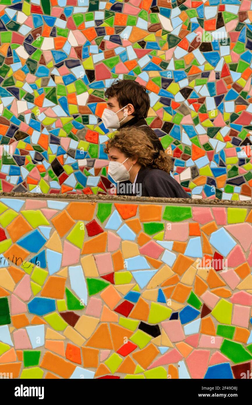 Dusseldorf, NRW, Germania, 19 marzo 2021. Due persone in maschere facciali FFP2/KN95 camminano oltre la parete a mosaico 'Rivertime' di Hermann-Josef Kuhna sulle rive del fiume Reno a Dusseldorf, capitale della NRW. È probabile che le misure di blocco aumenteranno ancora una volta in Germania, dal momento che il tasso di incidenza di 7 giorni salirà verso il punto cruciale di interdizione di 100 abitanti/100.000. Mentre oggi Dusseldorf ha un prezzo relativamente buono a 63, la Germania ha complessivamente visto aumentare i numeri a 95.6 Foto Stock