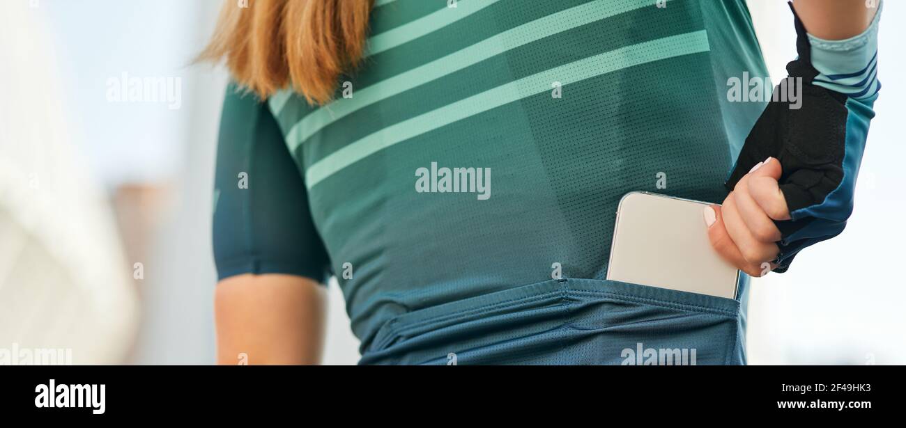 Intestazione del sito web di primo piano di professionale femminile ciclista in sportswear che mette il suo telefono cellulare in una tasca con zip di abbigliamento Foto Stock