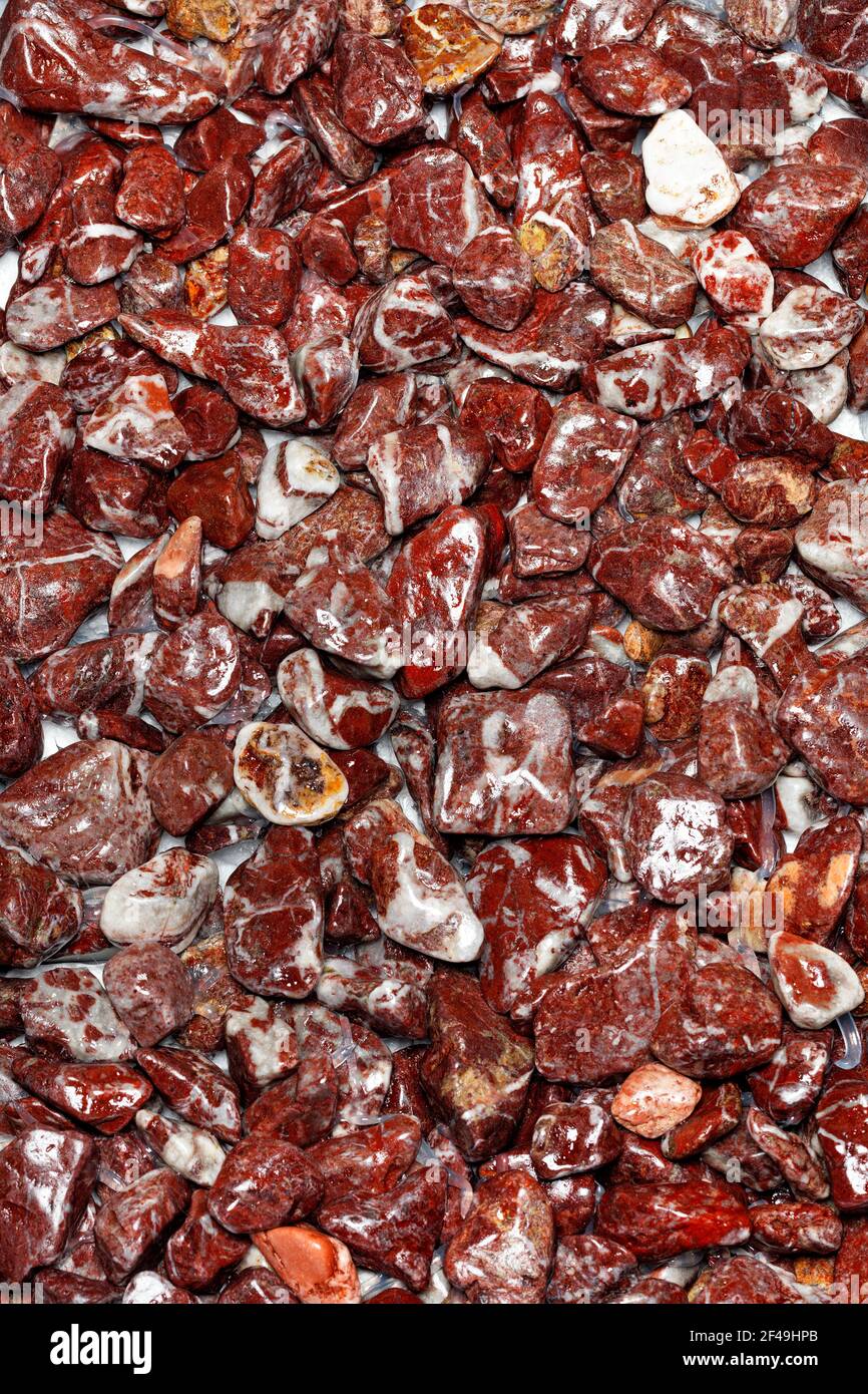 Bella texture di granito rosso bagnato in forma di ghiaia fine in pezzi lucidati, arrotondati e lucidati. Fotografia a colori verticale, primo piano. Foto Stock